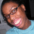 Pixelated close-up of a person's face with brown skin tone, dark hair, and light blue clothing against gray and black background.