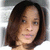 Pixelated portrait of a person with shoulder-length dark brown hair, light skin tone, and neutral expression against blurred background.