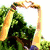 A person in a green shirt and blue capris forms a heart shape with hands above their head on a grassy hill under a bright sky.