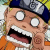 Pixelated cartoon character with wide eyes, open mouth showing teeth and tongue, wearing a blue-gray cap and orange clothing against a blurred background.