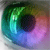 Pixelated circular icon with a central dark pupil surrounded by a gradient iris transitioning from green to blue to purple, set against a blurred background.