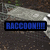A pixelated image shows a raccoon lying on the ground under a white sheet, with blue text reading "RACCOON!!!" overlaid.