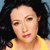 A pixelated close-up of a person with dark hair wearing a yellow top against a blue background.