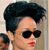 Pixelated close-up of a person with short dark hair, wearing dark sunglasses and red lipstick, against a light background.
