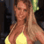 Static pixelated image of a woman in a yellow bikini top holding a green object, with brown hair and visible facial features against a dark background.