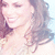 Pixelated close-up of a smiling person with long dark hair, light skin tone, and closed eyes against a pale background.