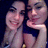 Two women pose together in a dark background, one resting her chin on her hand while the other smiles broadly.