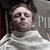 A pixelated grayscale image shows a person with short dark hair wearing a white shirt, positioned against a dark background with partial text visible on the right.
