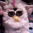 Pixelated image of a white Furby with large black eyes and a yellow nose, next to red pixelated text on a black background.