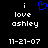 A black background displays white pixelated text reading "i love ashley 11-21-07" with a blue heart symbol above the word "love" in one view, and without the heart symbol in another view.