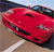 Red sports car with black accents on a road, viewed from a low angle with a blurred background.