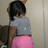 A pixelated image shows a person with short dark hair wearing a gray crop top and pink pants, standing against a light-colored wall.