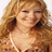 Pixelated image of a person with light brown hair wearing a white top, closed eyes, and a neutral expression against a plain background.