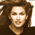 Pixelated close-up of a person with long brown hair, light skin, and a neutral expression against a dark background.