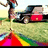 A pixelated static image shows a figure in dark clothing holding an object above their head, standing on grass near a vehicle with red and black elements.