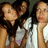 Three people with dark hair and light skin pose closely together, two wearing white tops against a muted background.