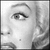 Black-and-white pixelated image of a woman's face with visible eye, nose, mouth, and hair; two lines of stylized text below.
