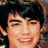 Pixelated close-up of a person with dark hair, closed eyes, and a wide open mouth showing teeth.
