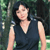 Pixelated image of a person with dark shoulder-length hair wearing a dark sleeveless top with a V-neckline against a blurred green background.