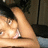 Pixelated image of a person with light skin tone wearing a white top, seated at a table with a blurred background.