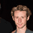 Pixelated static image of a person's head and shoulders against dark background with visible dithering and anti-aliasing artifacts.