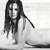 Pixelated grayscale image of a figure with long dark hair, wearing a light-colored garment, standing against a plain background.