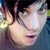 Pixelated close-up of a person's face with dark hair, light skin tone, and visible eyes, nose, mouth, and ear against a blurred background.