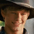 Pixelated close-up of a person wearing a dark wide-brimmed hat, light-colored shirt, and dark jacket with visible collar.