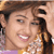 Static 50x50 pixel icon showing a close-up of a person with brown hair and light skin, wearing a yellow top with white patterns, smiling broadly with visible teeth against a blurred background.