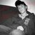 Black-and-white animated icon of a person in dark clothing and cap sitting on a couch with red patterned background.