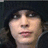 A pixelated portrait of a person with long hair and a dark hooded garment against a black background, with red text elements surrounding the image.