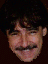 A pixelated close-up of a person with dark hair and a mustache, showing two sequential facial expressions against a dark background.