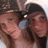 Two people in close proximity, one wearing a dark cap and the other with light brown hair, both with neutral expressions against a blurred background.