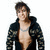 Pixelated static image of a person with dark hair wearing an open black jacket over a light-colored shirt and silver chain necklace.
