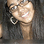 A person with long dark hair, glasses, and large hoop earrings smiles broadly in a pixelated image.