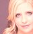 Pixelated close-up of a person's face with light-colored hair, visible eyes, nose, and mouth against a soft pinkish background.