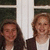 A static image of two women standing side-by-side in front of a white-framed window with greenery visible outside.