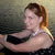 A woman with light brown hair in a ponytail wears a black sleeveless top with white polka dots and a white necklace, positioned against a gradient background.