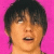 Pixelated close-up of a person with dark hair against bright pink background, mouth open in mid-expression.