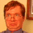 Pixelated image of a person with brown hair and glasses, split into two sections: left shows the upper body against a beige wall with framed art; right displays text on black background.