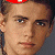 A pixelated image of a person with light brown hair and blue eyes, wearing a red headband on the left side against a dark green background with bright green text.