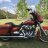 Pixelated static image of a person riding a motorcycle in an outdoor setting with trees and sky visible.