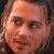 Pixelated close-up of a person's face with light skin tone, visible eyes, nose, mouth, and partial hair, set against a dark background.