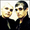 Two individuals in dark clothing with one wearing a striped tie, positioned side-by-side against a light background.