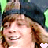 Pixelated image of a person with light brown hair wearing a dark blue cap, smiling broadly with visible teeth and closed eyes in two side-by-side frames showing slight facial movement.