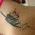 A tattoo of a black and red anime-style character with flowing hair on light skin, partially visible against a blurred background.