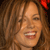 A pixelated close-up of a person with long brown hair, a red bow on the right side, and a wide open mouth showing teeth.