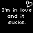 Black background with white pixelated text and a heart symbol, displaying 'I'm in love I'm in love and it sucks.' repeated twice.