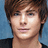 Pixelated close-up of a person with brown hair against a blue background, wearing a dark top.