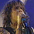 A pixelated figure with long brown hair and a light-colored top against a blue background, showing partial facial features and a vertical light streak.